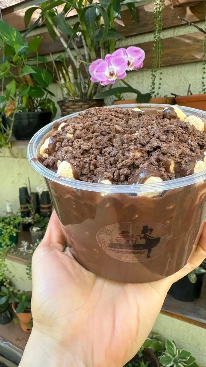 Tigela de sobremesa com cobertura de chocolate e biscoitos em um jardim com orquídea rosa ao fundo.