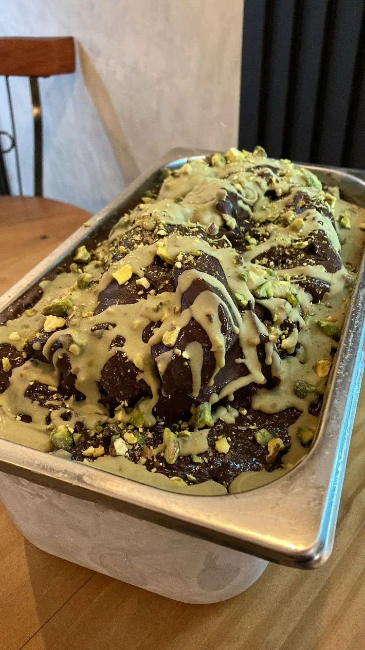 Sobremesa de chocolate com calda verde e pedaços de pistache em uma bandeja de metal.