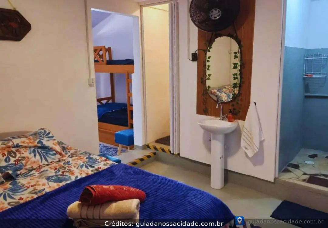 Quarto com cama de casal florida, beliche, pia com espelho e toalhas dobradas.