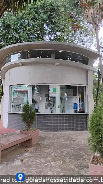 Quiosque moderno com fachada de vidro e telhado curvo em área arborizada.