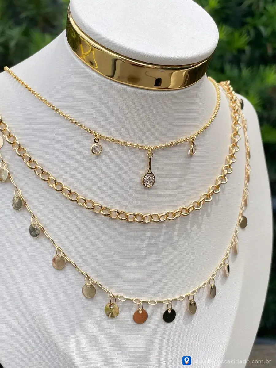 Colares dourados em manequim, incluindo gargantilha lisa e correntes com pingentes circulares.