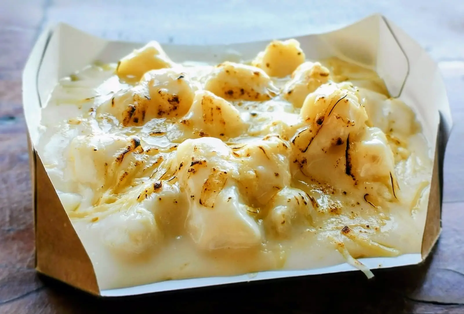 Porção de nhoque com molho cremoso e gratinado em caixa de papelão.