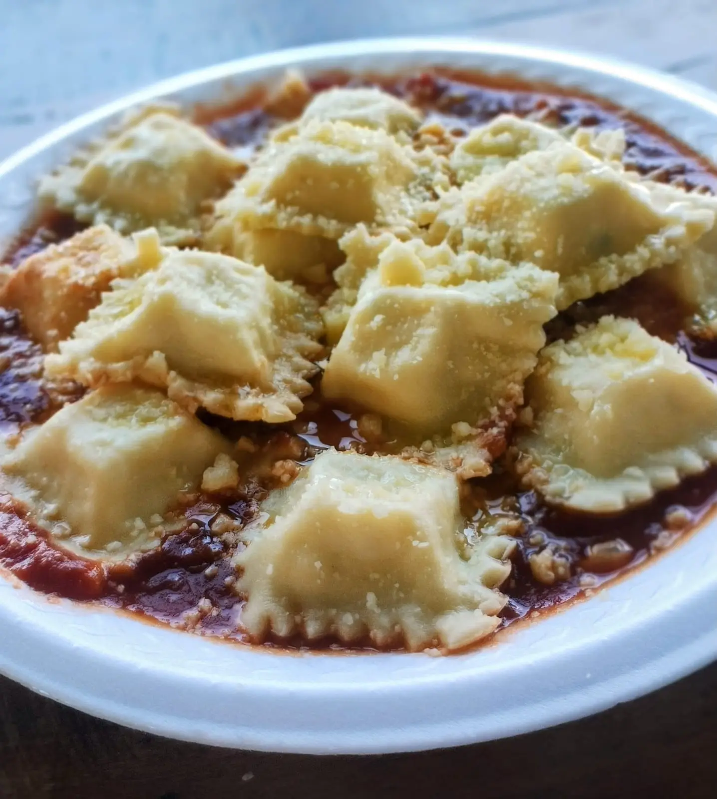 Prato de raviolis cobertos com queijo parmesão sobre molho de tomate.