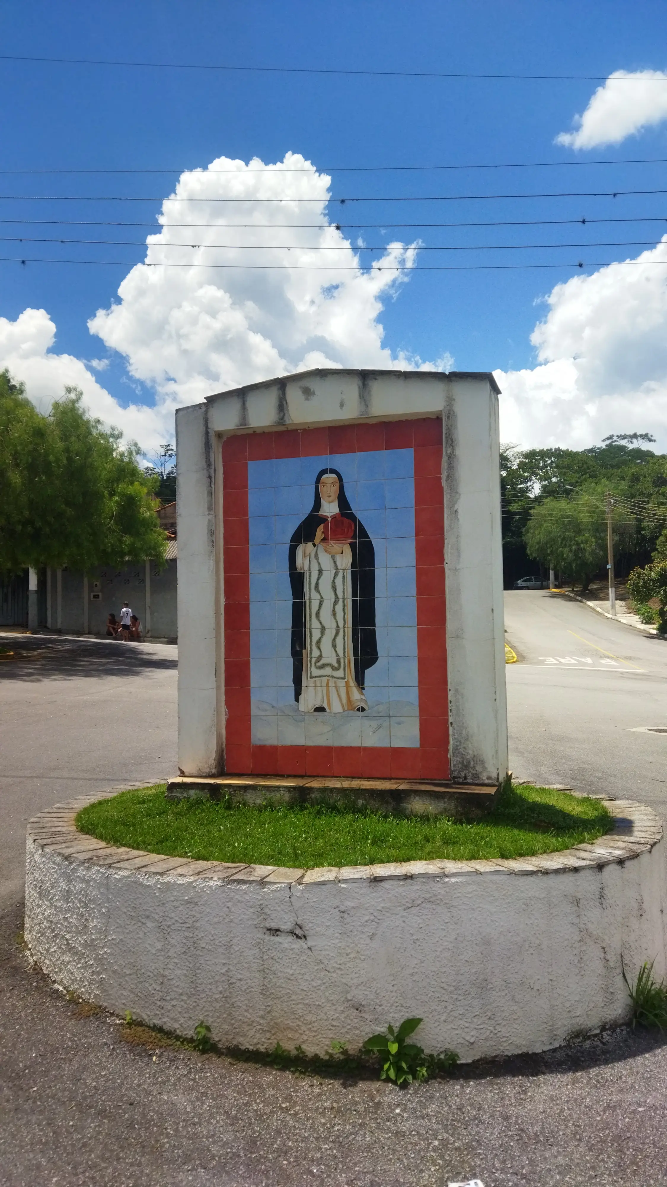 Mosaico de santa em pedestal circular com céu azul ao fundo.