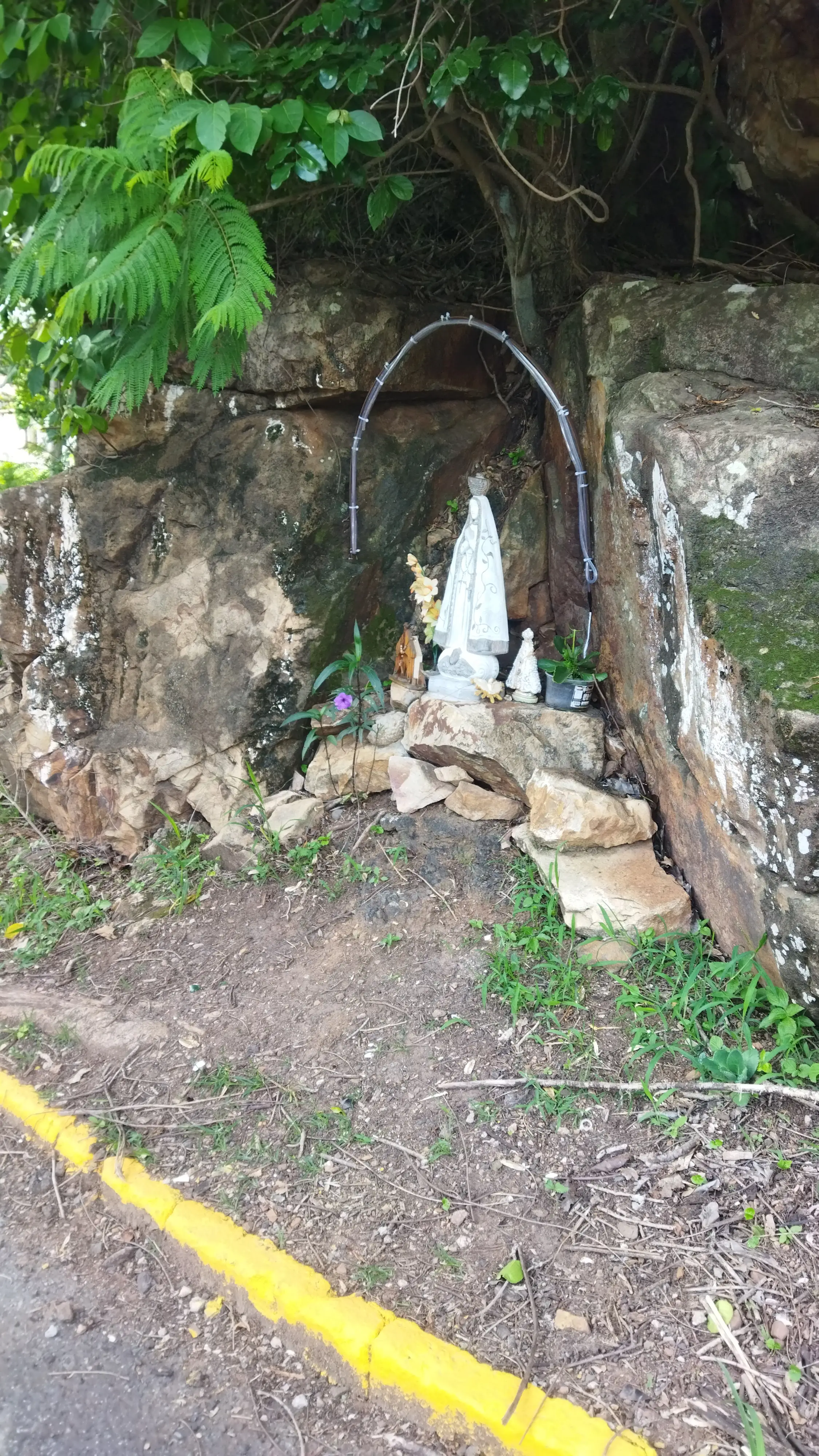 Pequeno altar com imagens religiosas em meio a pedras e vegetação.