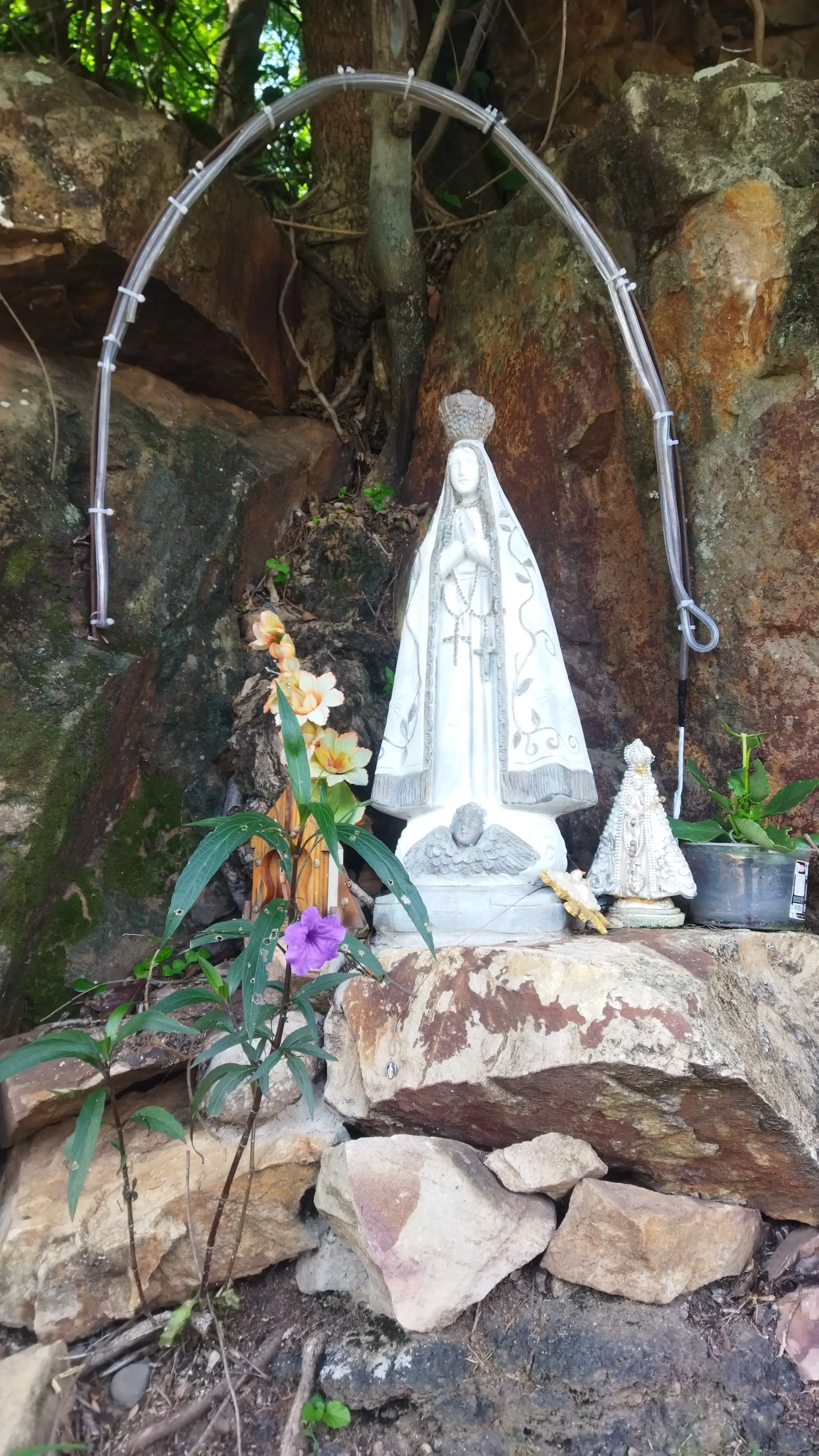 Estátuas de figuras religiosas em altar de pedra com flores e vegetação ao redor.