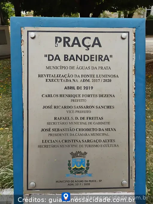 Placa em praça pública com informações sobre revitalização em Águas da Prata, nomes de autoridades e brasão da cidade.