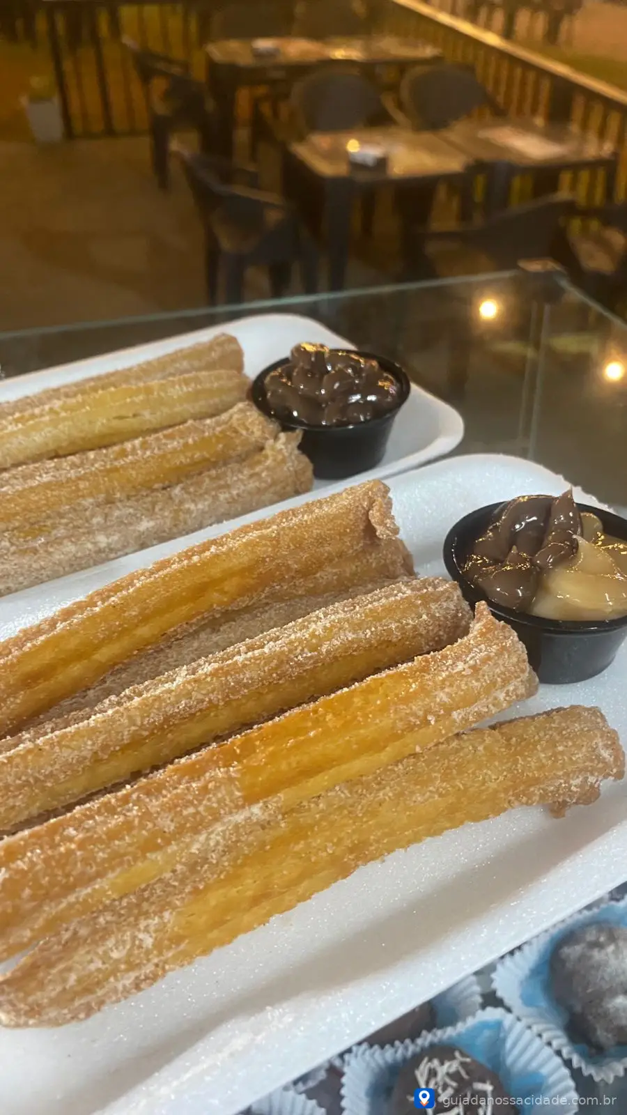 Churros cobertos com açúcar, acompanhados de chocolate e doce de leite em um restaurante ao ar livre.