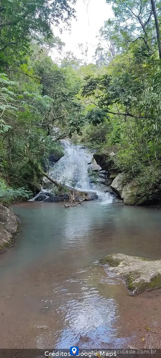 Cachoeira em meio à floresta com águas claras cercadas por vegetação e pedras.