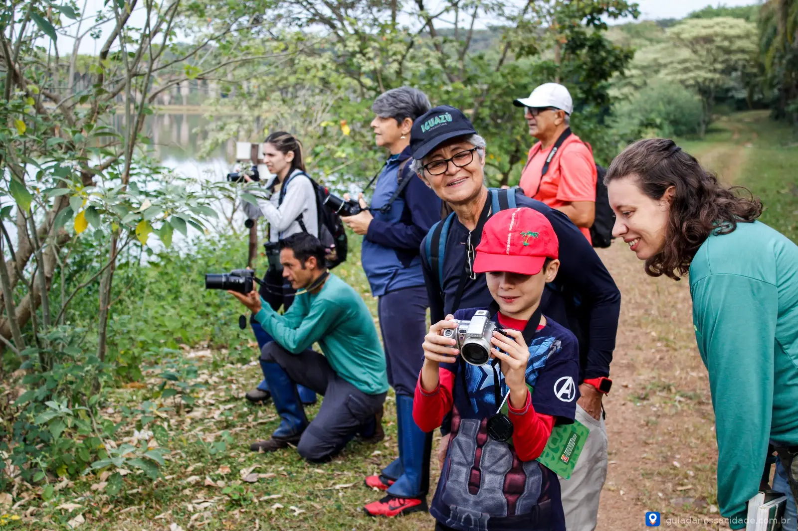 Grupo de pessoas com câmeras fotográficas observando a natureza em um parque arborizado.