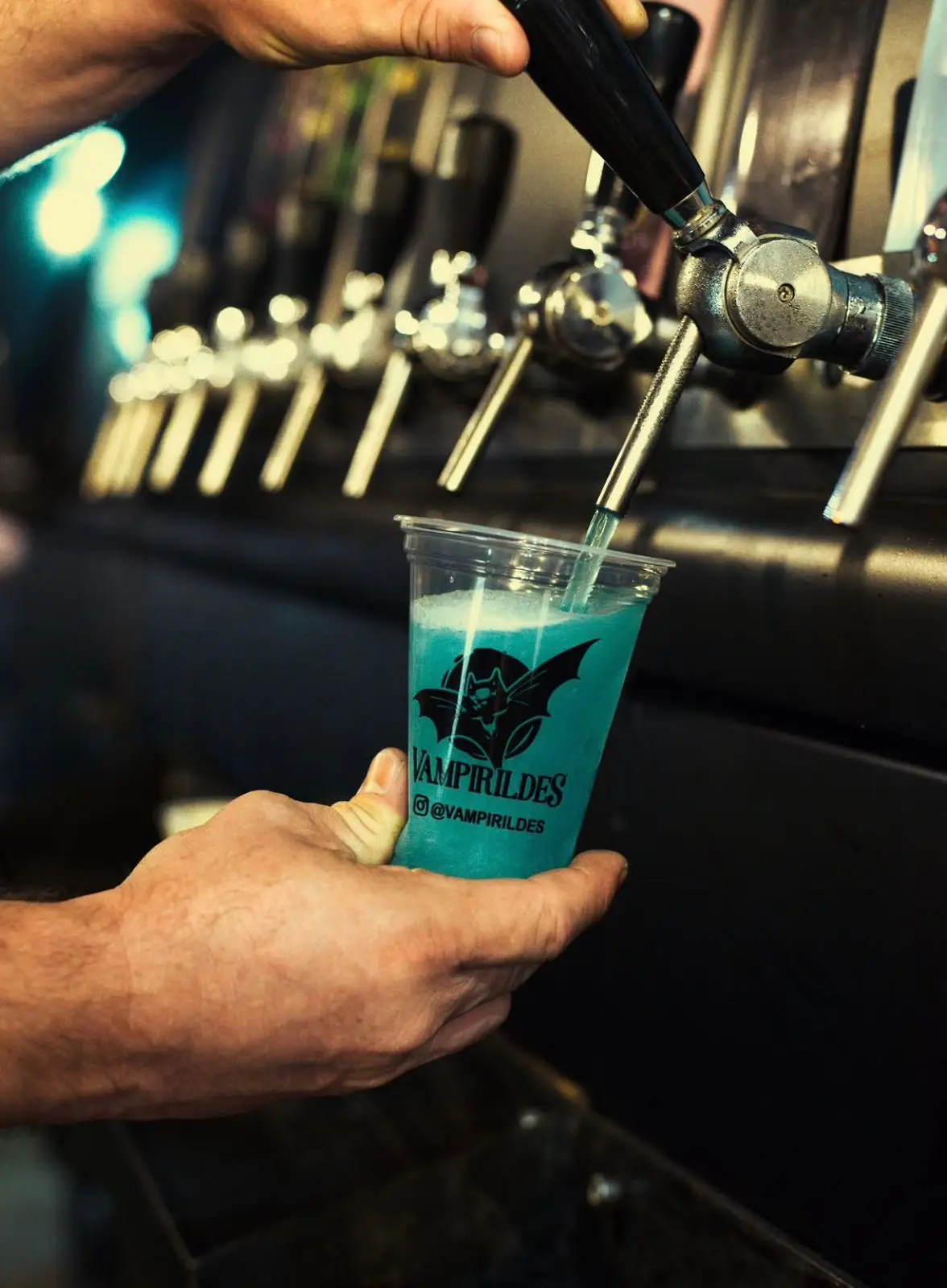 Pessoa enchendo copo com bebida azul em torneira de bar.