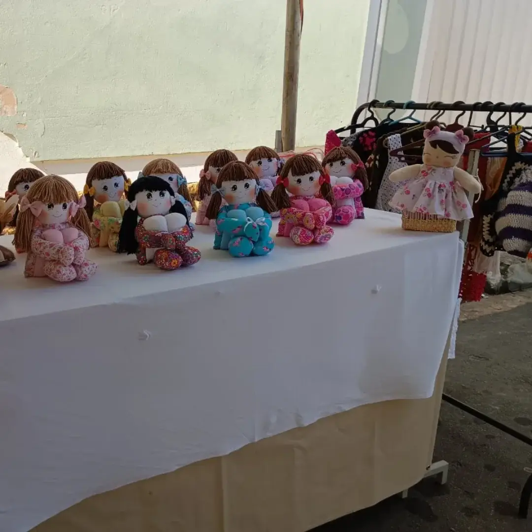 Expositor com bonecas de pano coloridas e bolsas de crochê penduradas.