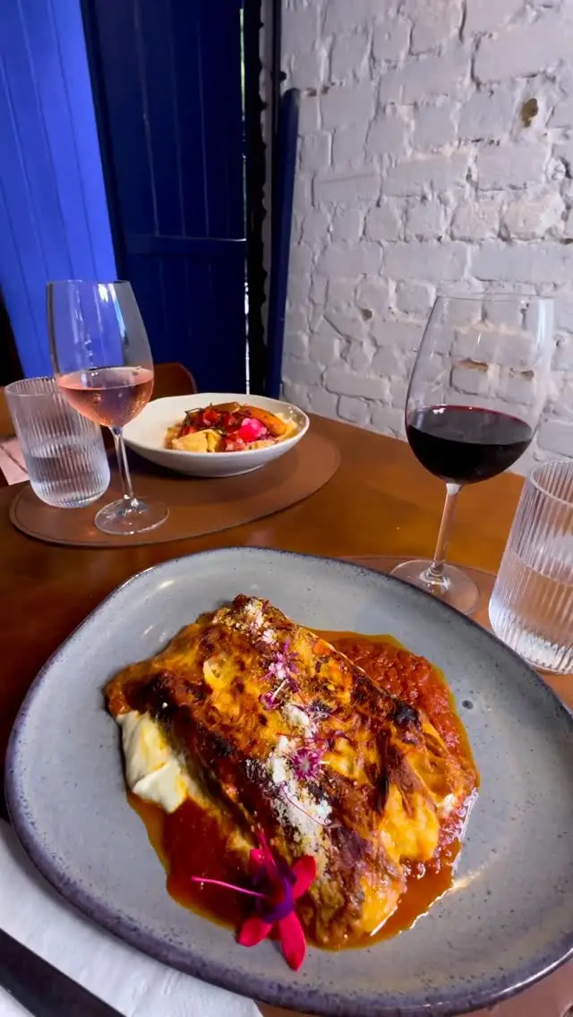 Massa gratinada em prato com flores, taças de vinho tinto e rosé sobre mesa de madeira.