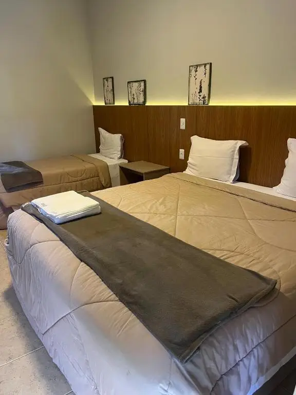 Quarto com duas camas, uma de casal e outra de solteiro, com decoração moderna e tons neutros.