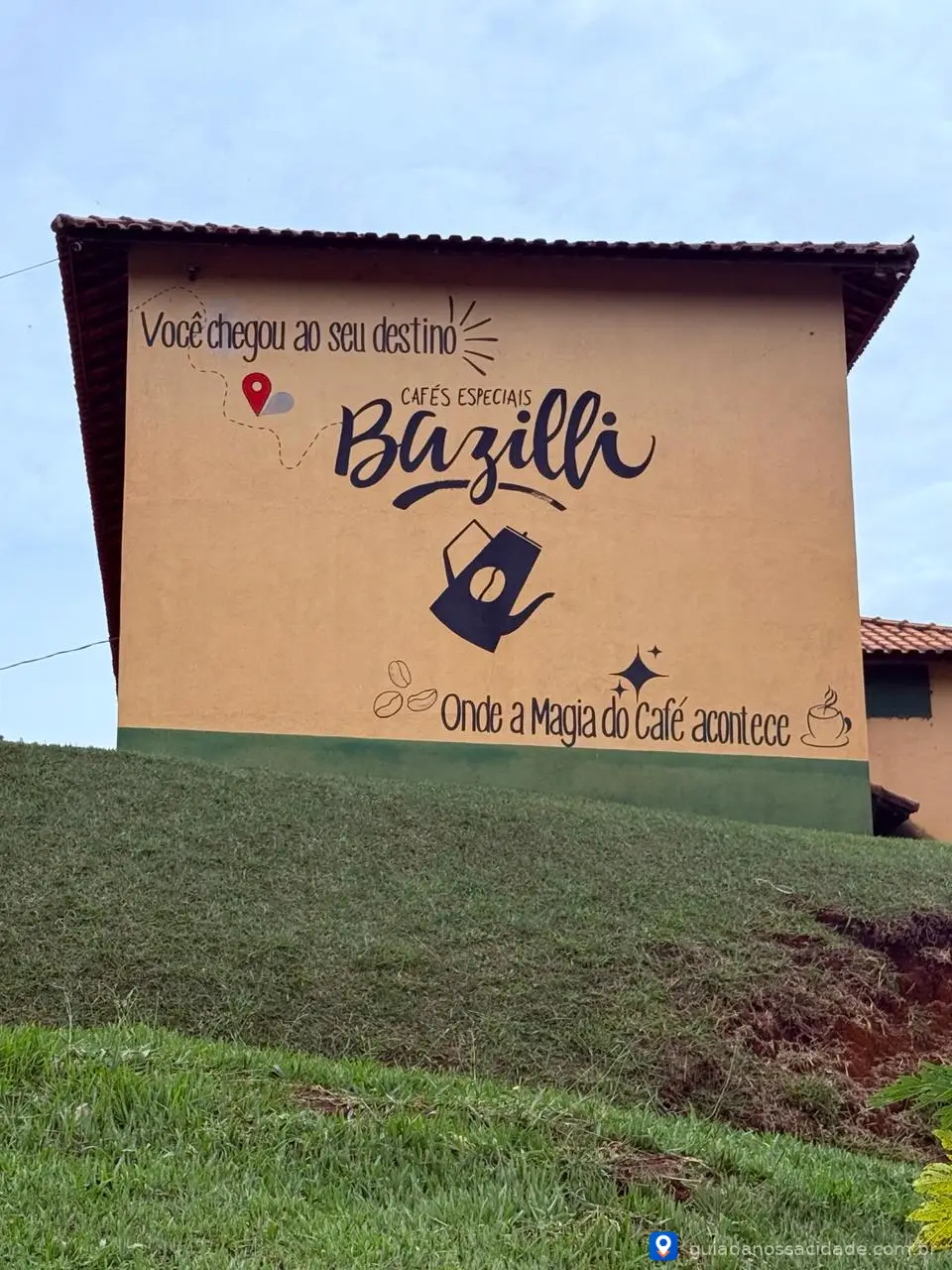 Paredão com pintura de café especial Bazilli em área gramada, frase sobre magia do café e ícones gráficos.