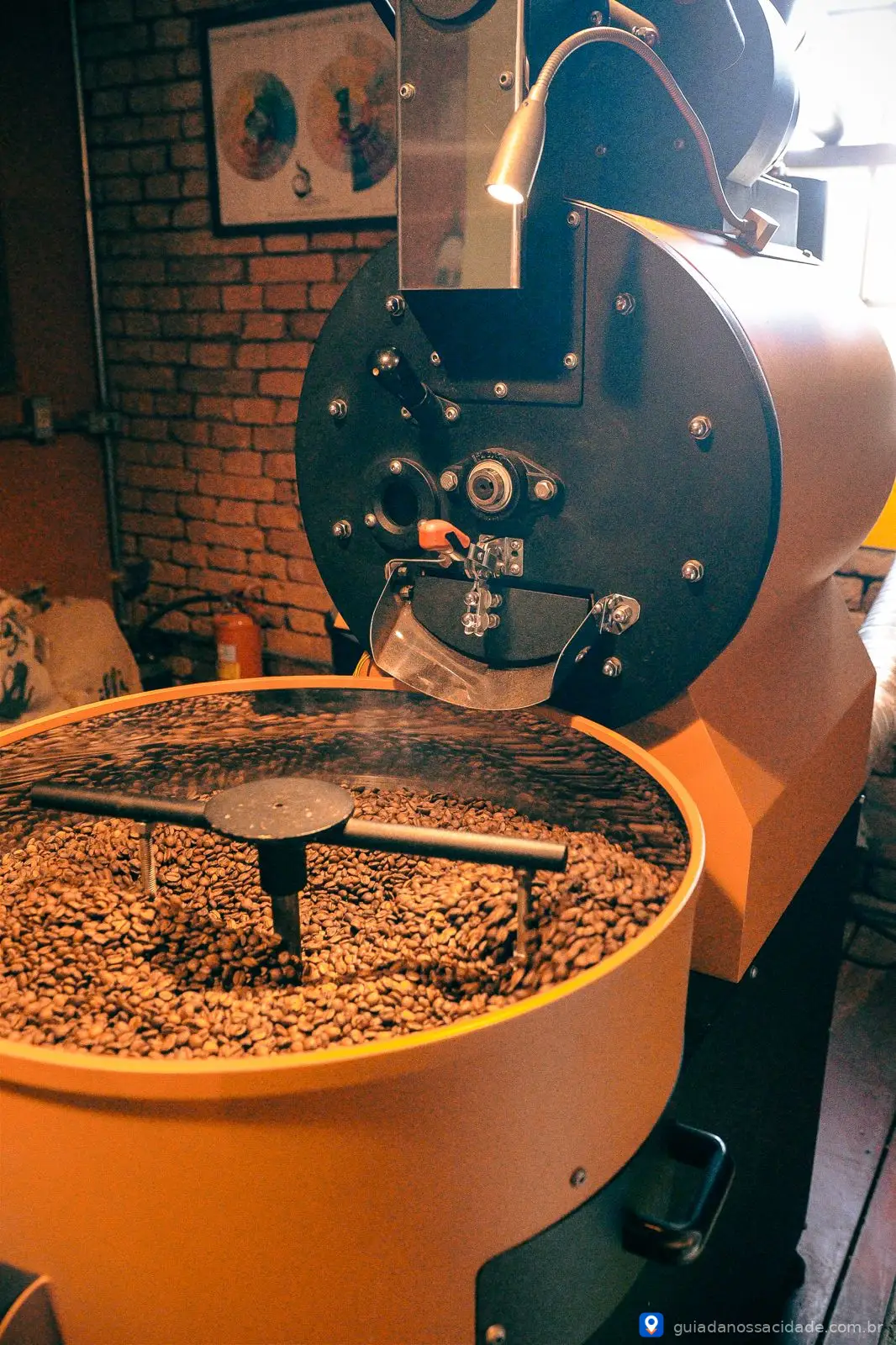 Torrador de café com grãos em processo de torrefação em ambiente de tijolos expostos.