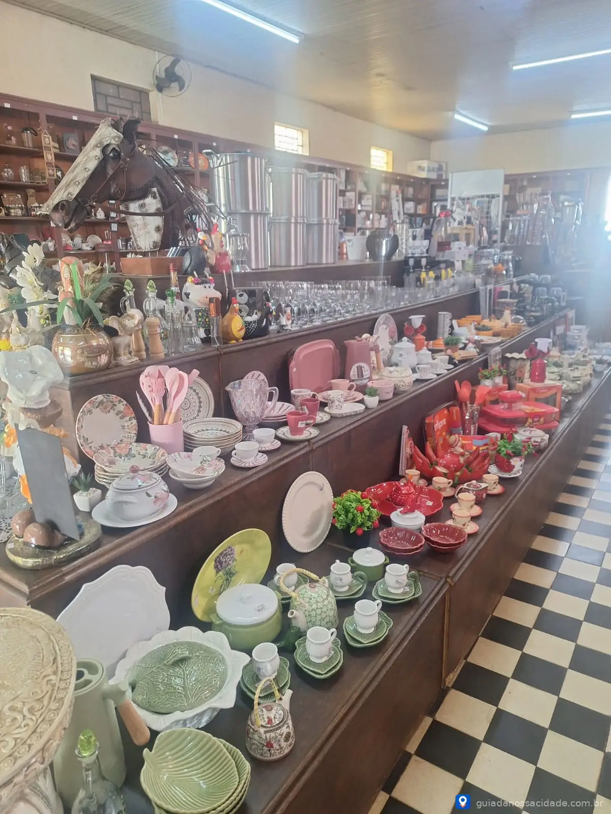 Loja com louças, utensílios de cozinha e decoração expostos em prateleiras, chão xadrez preto e branco.