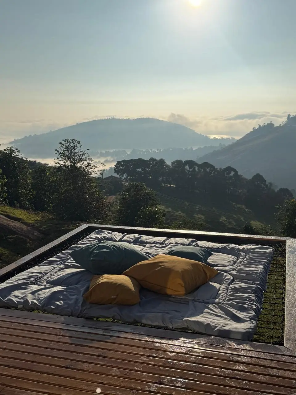 Espaço acolchoado com almofadas em deck de madeira com vista para montanhas ao amanhecer.