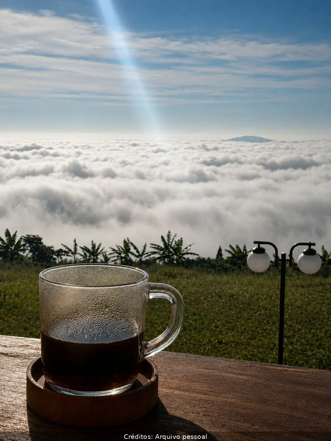 Copo de café em mesa de madeira com vista para nuvens e céu azul.