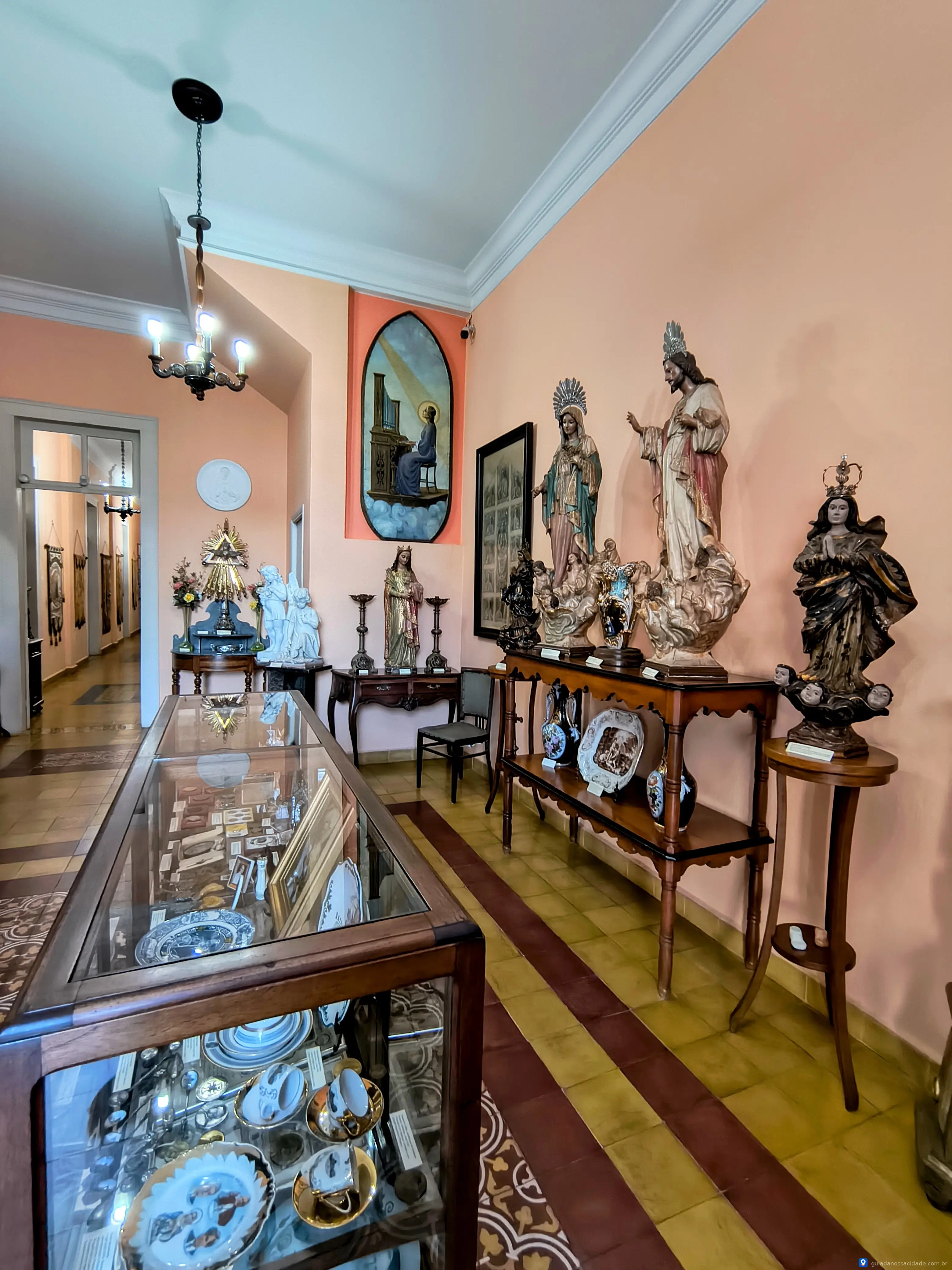 Sala com estátuas religiosas e vitrine com porcelanas em ambiente de museu.