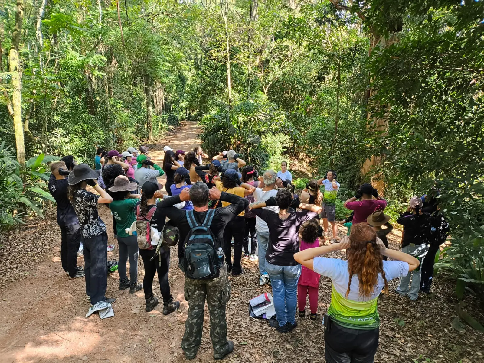 Grupo de pessoas faz exercício ao ar livre em trilha cercada por vegetação densa.